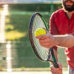 Mann hält Tennisschläger und Ball auf einem Tennisplatz, und immer bereit für eine dienen – © valentinrussanov - istockphoto.com - 1300812835