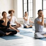 Full length group of young fit motivated focused multiracial people sitting in lotus position, practicing Alternate Nostril Breathing, finishing yoga session indoors with nadi shodhana pranayama. – © fizkes - istockphoto.com - 1262414071