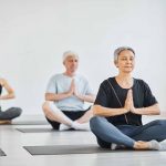 Senior people sitting on mats in lotus position with eyes closed and meditating during yoga in class – © SeventyFour - istockphoto.com - 1349259747